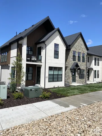 Contemporary exterior featuring a stone and stucco facade, wood-finish siding, black-framed windows, and a second-story balcony