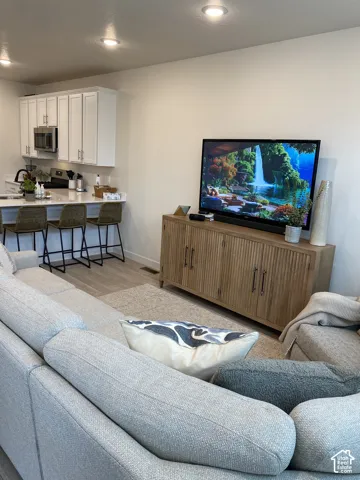 Recessed ceiling lighting, wood-finish flooring, white cabinetry with dark pulls, light-colored countertops, and stainless steel appliances