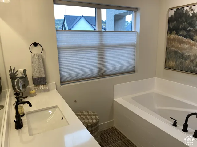 Built-in soaking tub with matte black fixtures, single vanity with a rectangular undermount sink, and a white countertop
