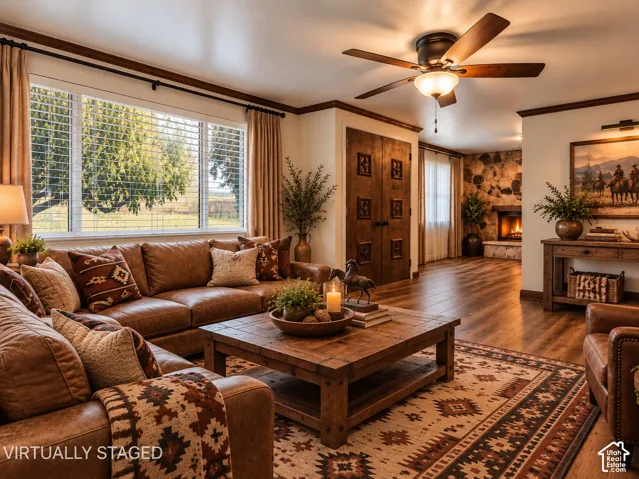 Wood-finish flooring, stone-accented fireplace, decorative paneled wood doors, crown molding, and a ceiling-mounted light fixture with fan