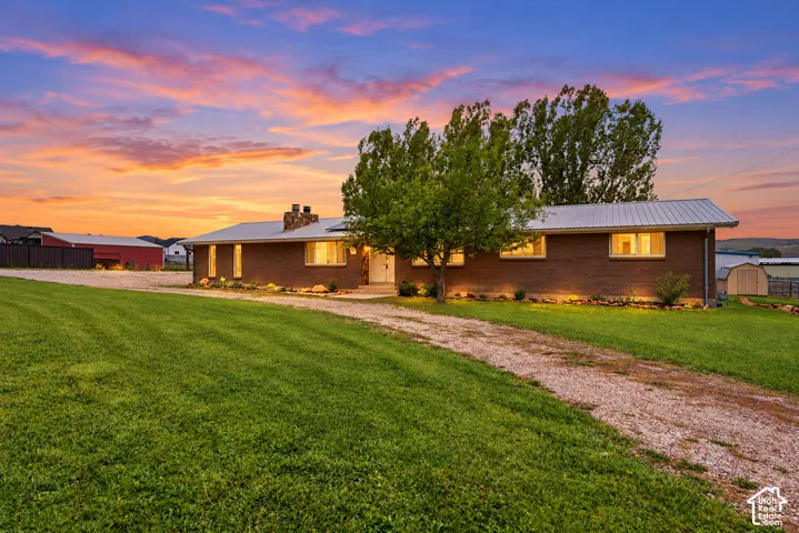 Single-story brick exterior featuring a metal roof, stone-accented chimney, gravel driveway, and manicured lawn