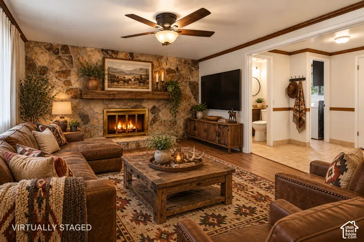Living room featuring an expansive stone-accent wall, wood-burning fireplace with a timber mantel, and a ceiling fan with integrated lighting
