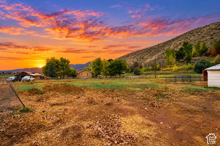 Expansive acreage featuring mature trees, perimeter fencing, mountain backdrop, and outbuildings