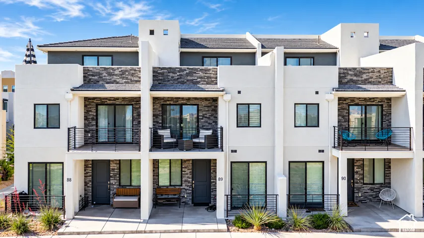 Contemporary multi-story exterior featuring smooth stucco finish, stone veneer accents, upper-level balconies with horizontal cable railings, and dark-framed sliding glass doors