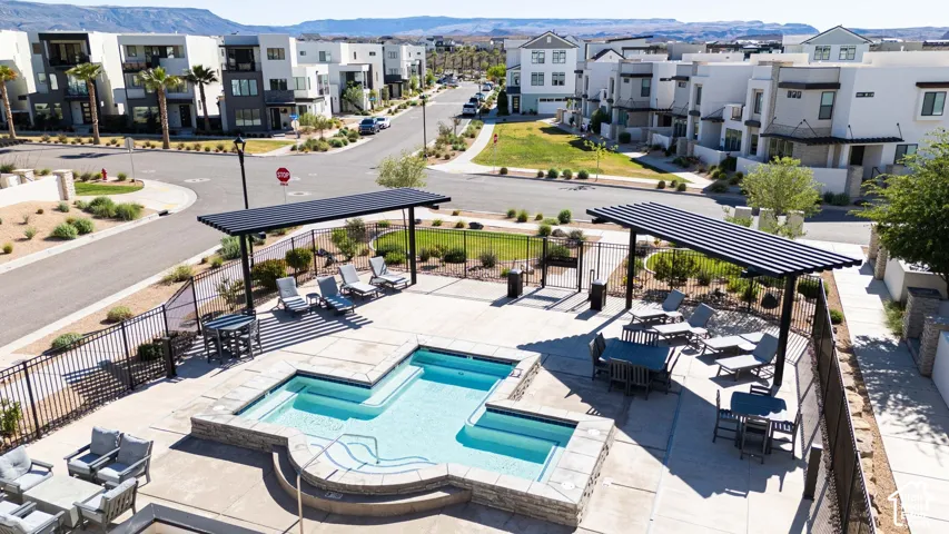 Community pool area featuring an in-ground swimming pool with stone-veneer border, concrete decking, metal perimeter fencing, and two integrated pergola structures