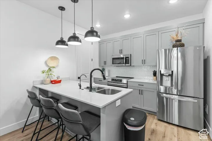 Kitchen featuring light-toned cabinetry, solid-surface countertops, stainless steel appliances, herringbone-pattern backsplash, and wood-finish flooring