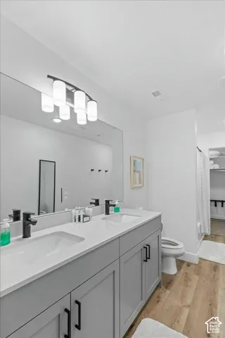 Dual-vanity cabinetry with shaker-style doors, light-toned countertop, integrated dual sinks, matte black hardware, and wood-finish flooring