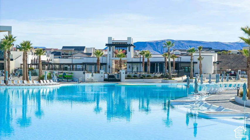 Large-scale swimming pool featuring a beach-entry perimeter, surrounding hardscaping, and palm tree landscaping against a mountain backdrop
