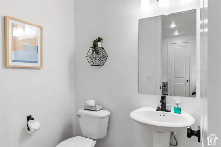 Pedestal sink with matte black faucet, wall-mounted mirror, three-light vanity fixture, and matte black hardware