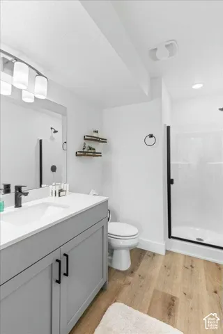 Bathroom featuring a gray vanity with a solid-surface countertop, matte black hardware, wood-finish flooring, and a walk-in shower with a matte black frame