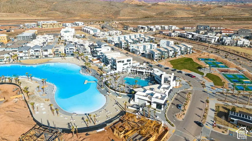 Aerial perspective of the community featuring an expansive blue-water swimming lagoon, a secondary pool complex, multi-use sports courts, and desert mountain topography