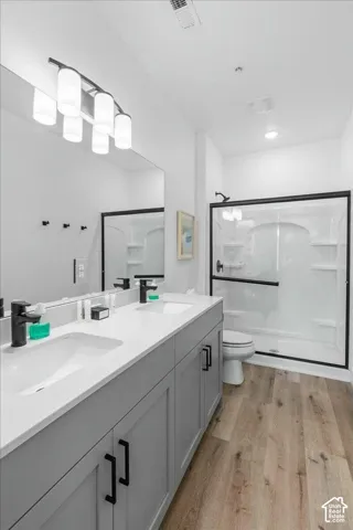 Dual-sink vanity with light-tone cabinetry, quartz countertops, matte black plumbing fixtures, wood-finish flooring, and a glass-enclosed shower with a matte black frame