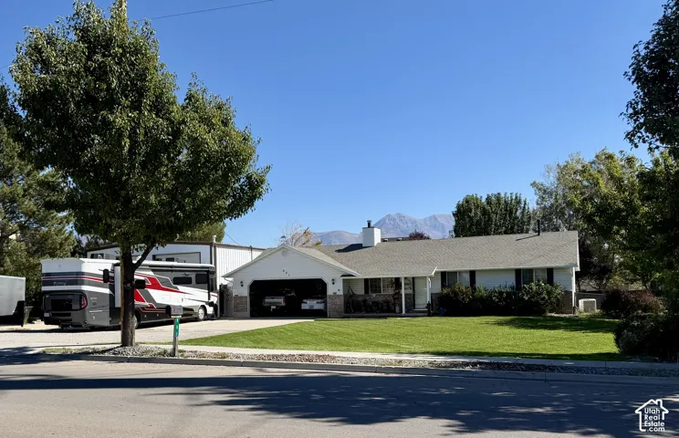 Single-story residence featuring a two-car attached garage, expansive paved parking area, manicured lawn, and mountain backdrop