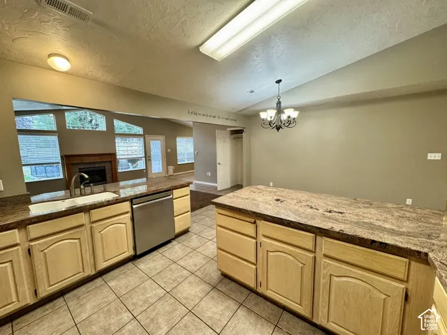 Kitchen featuring stone-patterned countertops, wood-finish cabinetry, stainless steel dishwasher, tile flooring, and vaulted ceiling