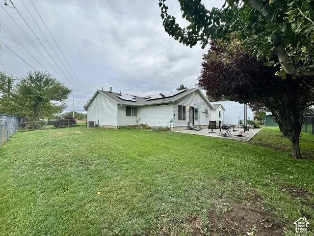 Exterior view featuring white siding, roof-mounted solar panels, concrete patio, and fenced backyard with mature trees