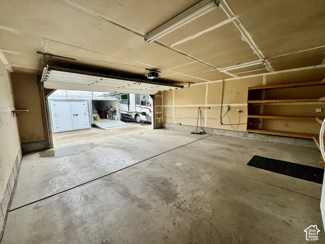 Attached garage featuring concrete flooring, built-in wooden shelving, and an automatic door opener