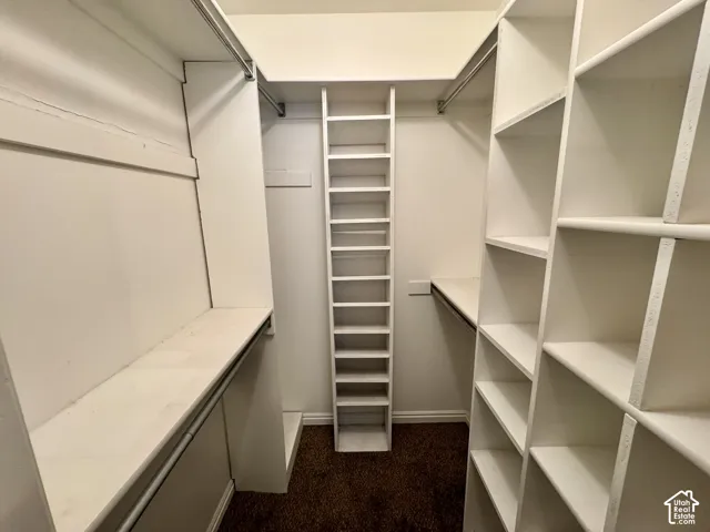 Walk-in closet featuring white built-in shelving, vertical storage cubbies, and integrated clothing rods