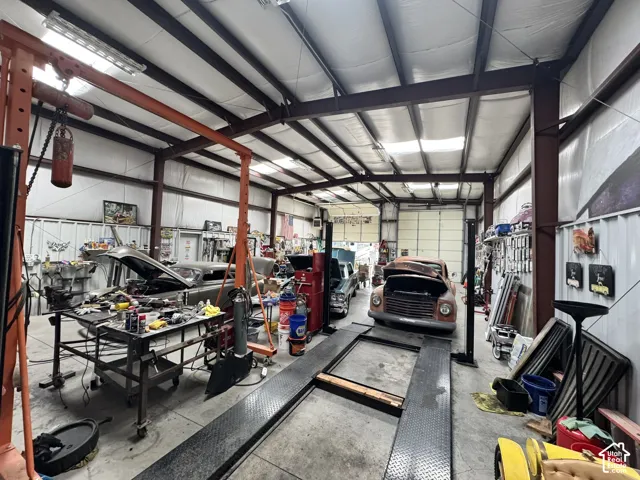 Spacious workshop featuring high-clearance metal beam framing, concrete flooring, integrated auto lift, and oversized overhead bay door
