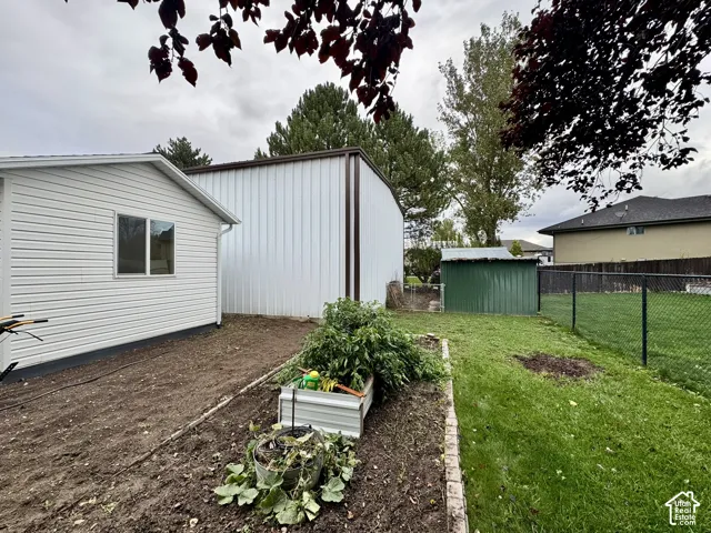 Exterior property featuring a detached metal structure, fenced yard, and a garden area with brick edging