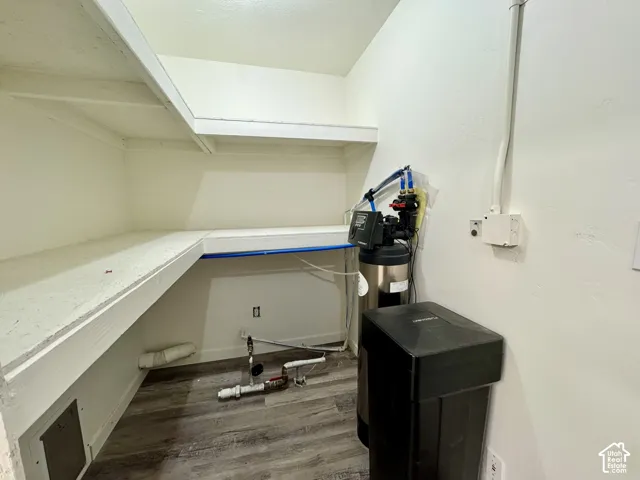 Utility area featuring custom wrap-around built-in shelving, wood-finish flooring, and a water softening system