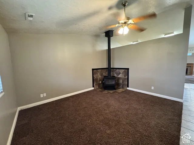 Vaulted ceilings, corner wood-burning stove with a tile surround, and an integrated ceiling fan with multi-light fixture