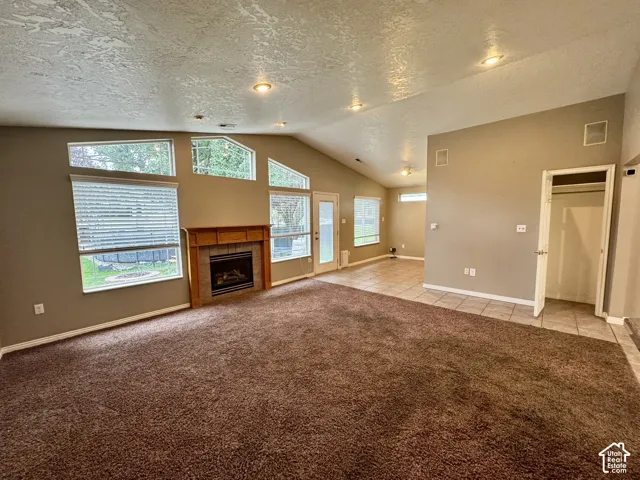 Vaulted ceilings featuring recessed lighting, fireplace with a wood mantle, multi-pane picture windows, and tile flooring