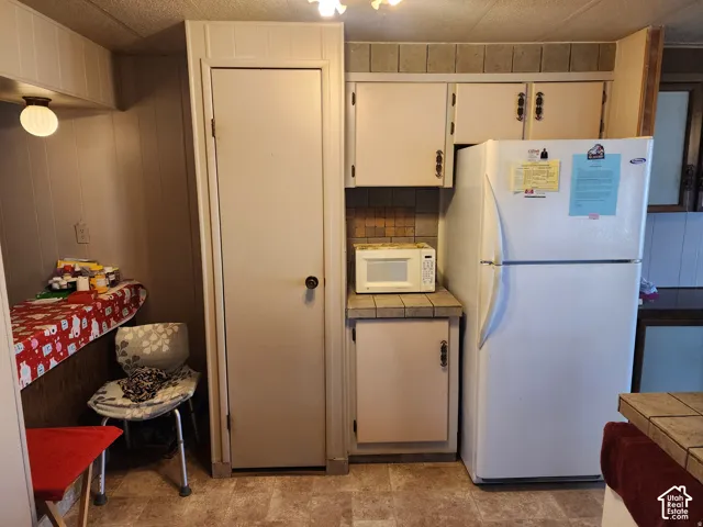 Kitchen area featuring light-toned cabinetry, tile backsplash, tile countertop, and a built-in pantry door