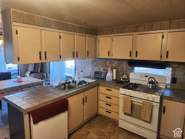 Kitchen featuring tile countertops, tiled backsplash, built-in cabinetry with decorative hardware, and integrated range hood