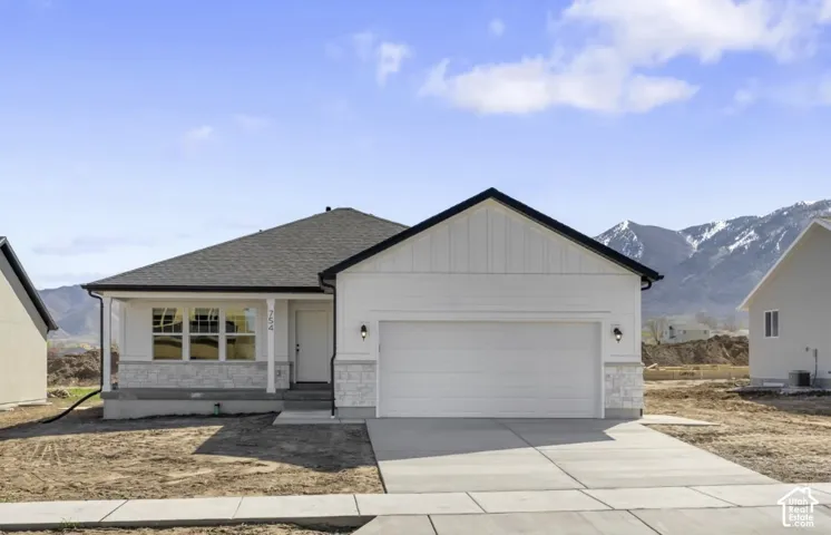 Single-story exterior featuring white board-and-batten siding, stone veneer accents, an attached two-car garage, and a covered front porch, set against a mountain backdrop