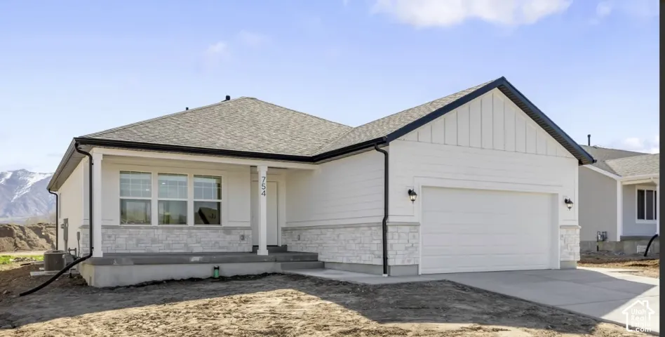 Single-story exterior featuring white horizontal siding, vertical board-and-batten accents, stone veneer wainscoting, a concrete porch, and a two-car garage