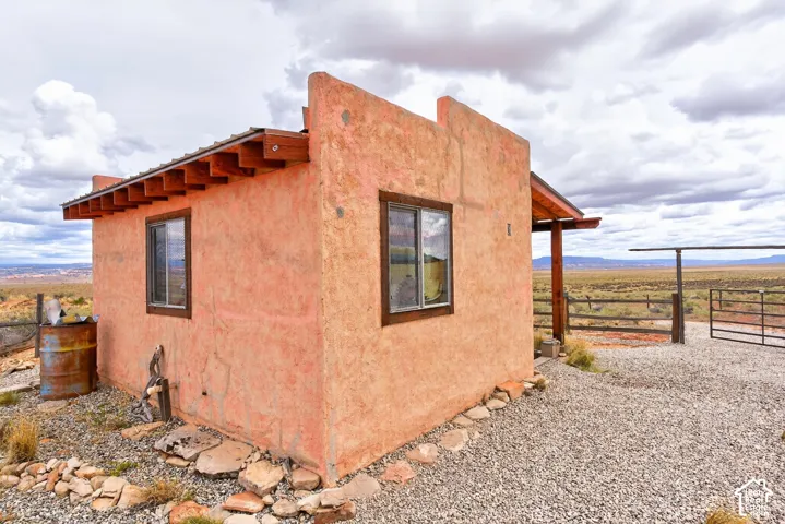 Stucco exterior with exposed wood rafters, wood-trimmed windows, gravel landscaping, and a fenced area with a metal gate