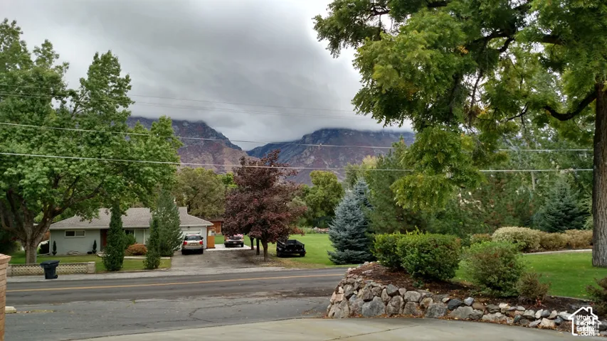 Extensive mountain backdrop with mature deciduous and evergreen trees, tiered stone landscaping, and manicured lawns