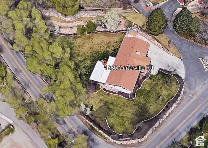 Aerial perspective of the property featuring a structured roofline, an attached white patio cover, and extensive perimeter landscaping defined by stone retaining walls