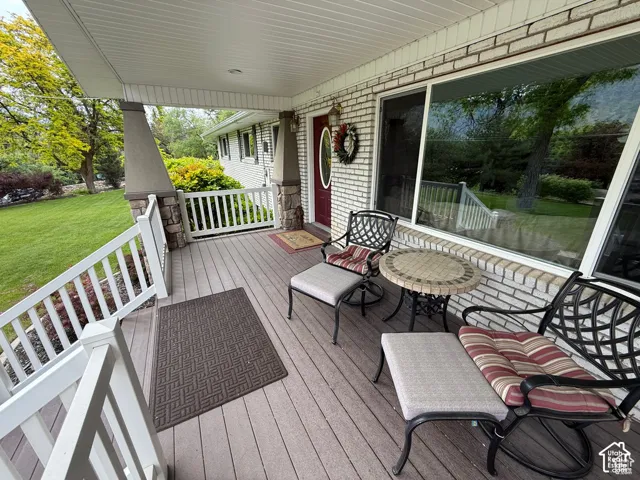 Covered front porch featuring composite decking, white railing, brick exterior cladding, and stone-accented support columns
