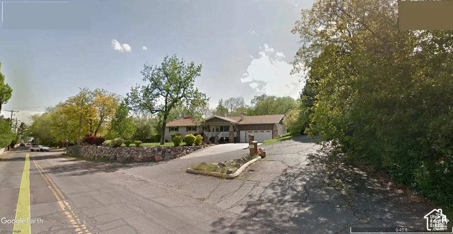 Exterior featuring a stone retaining wall, concrete driveway, attached multi-car garage, and established mature trees