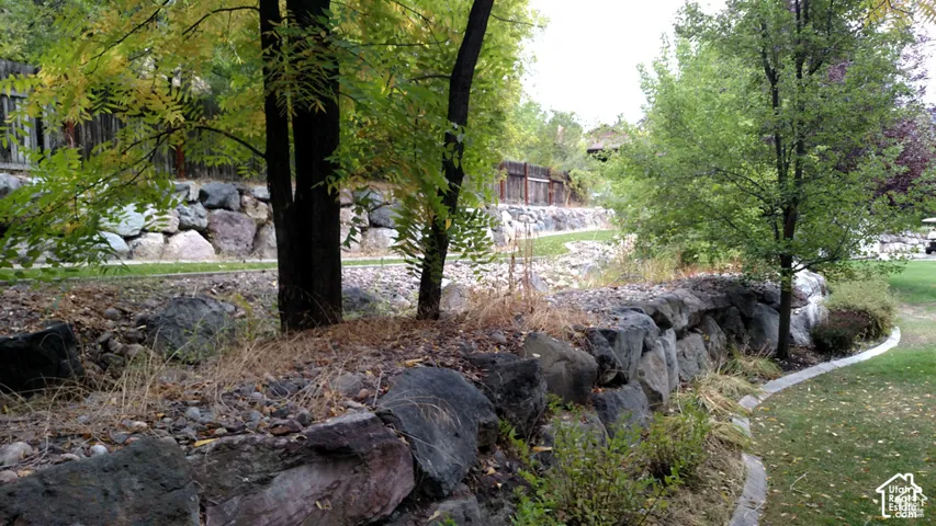 Terraced backyard featuring tiered natural stone retaining walls, mature deciduous trees, a manicured lawn, and stone edging