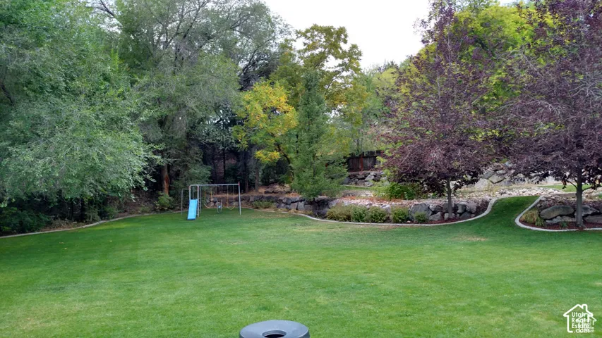 Expansive lawn featuring tiered rock landscaping, mature trees, and defined garden beds