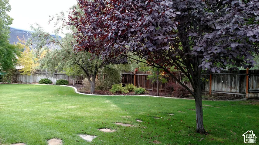Backyard featuring a manicured lawn, established shade trees, wood privacy fencing, stone-style garden curbing, and natural stone pavers