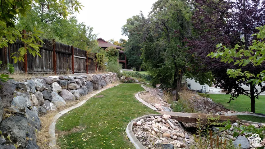Terraced backyard featuring a natural stone retaining wall, grass lawn, stone-lined dry creek bed, and a footbridge