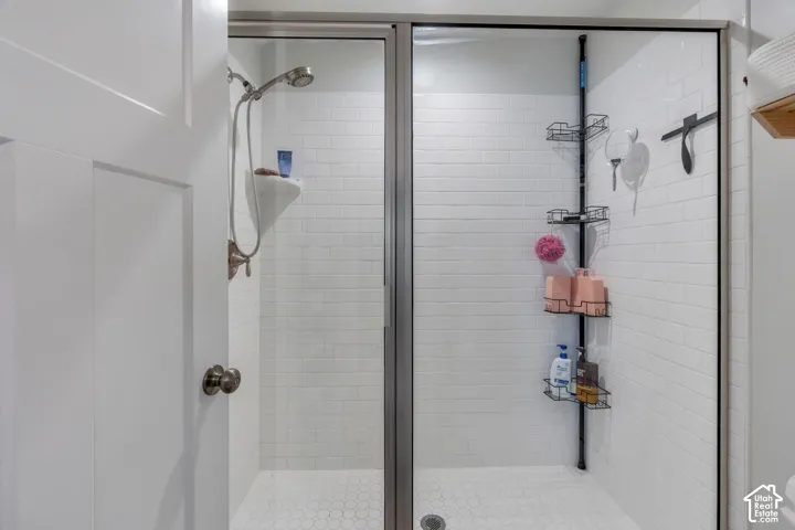 Walk-in shower featuring a glass enclosure with a metal frame, white subway-style wall tile, white hexagonal floor tile, and a multi-setting hand-held shower fixture