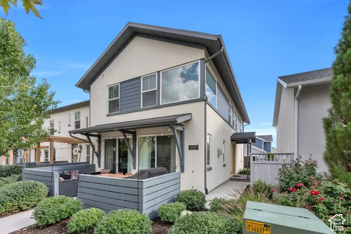 Two-story contemporary exterior featuring stucco siding, horizontal wood-finish lap accents, a private fenced patio, and oversized window configurations
