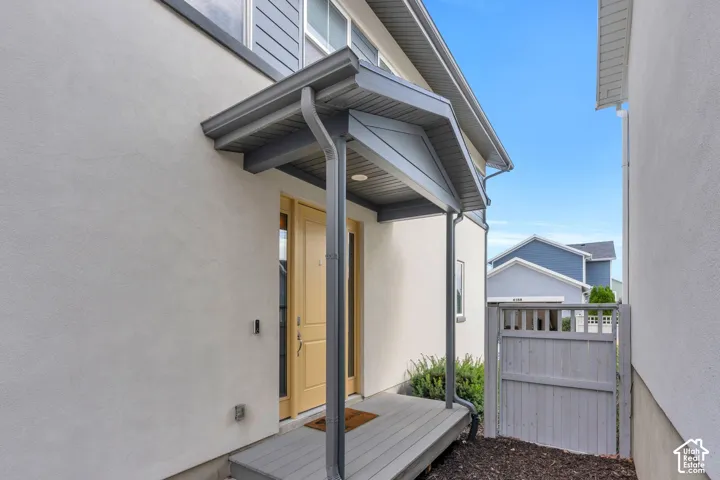 Exterior entrance featuring a covered front porch, smooth stucco siding, grey wood-finish decking, and a solid wood entry door with side windows