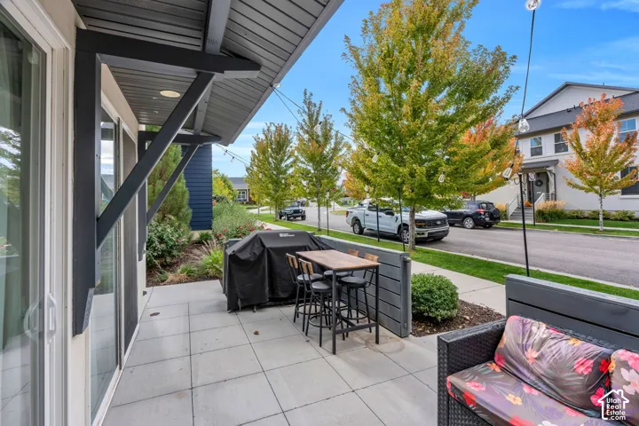 Covered concrete patio featuring dark structural support beams, horizontal privacy screening, and glass sliding door access