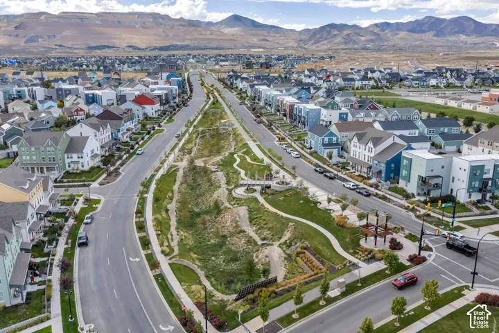 Aerial perspective of a planned community featuring a central landscaped corridor, paved pedestrian pathways, manicured green space, and a mountainous backdrop