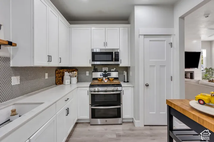 Kitchen featuring white cabinetry, light-toned composite countertops, a geometric mosaic tile backsplash, stainless steel appliances, and wood-finish flooring