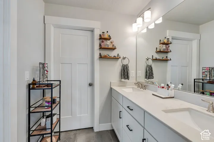 Double vanity featuring white cabinetry, light-toned stone-finish countertops, rectangular undermount sinks, matte black hardware, and an expansive wall-to-wall mirror