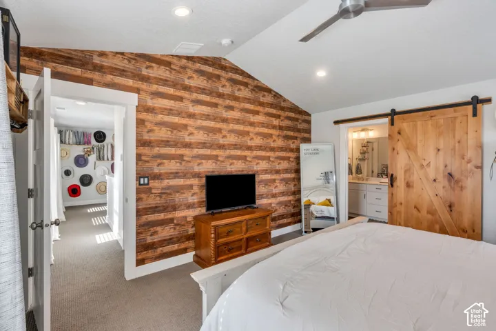 Vaulted ceiling with recessed lighting and a ceiling fan, featuring a prominent wood-plank accent wall and a sliding barn-style door