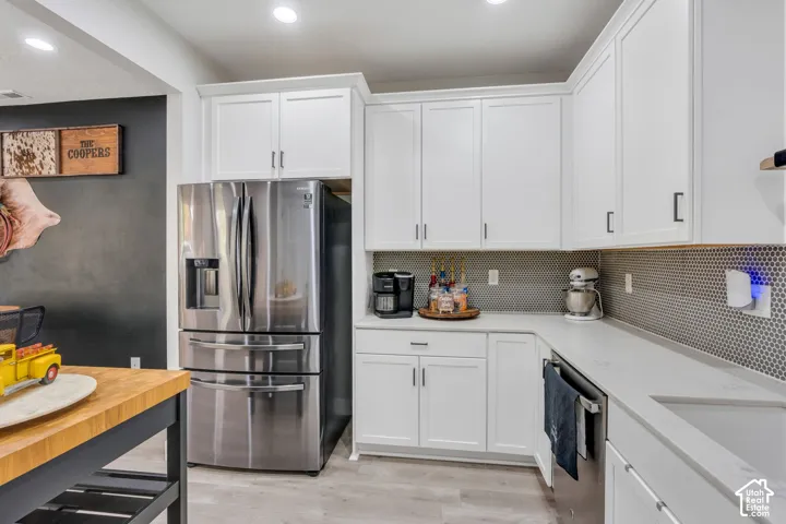 White shaker-style cabinetry, stainless steel refrigerator, stone-composite countertops, penny-round tile backsplash, and recessed lighting