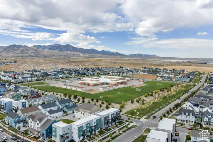 Aerial perspective of a suburban neighborhood featuring paved streets, multi-story residential structures, and expansive mountain scenery