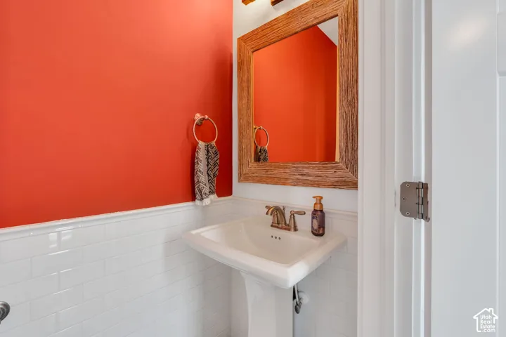 Pedestal sink with a dual-handle metal faucet, white subway tile wainscoting, and a wood-frame wall-mounted mirror
